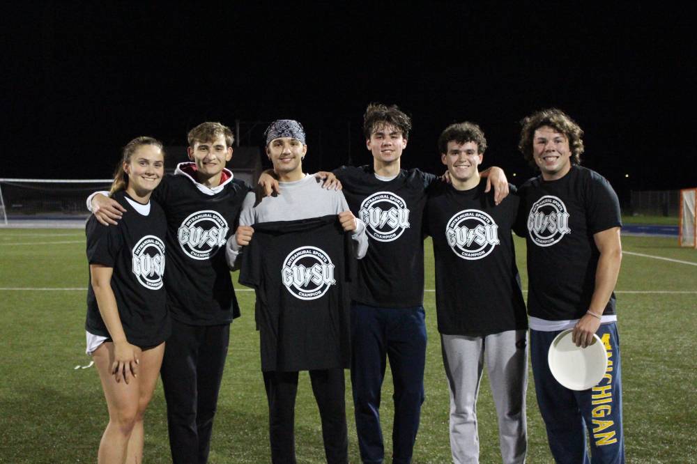 Students holding up and wearing championship shirts from a ultimate frisbee tournament